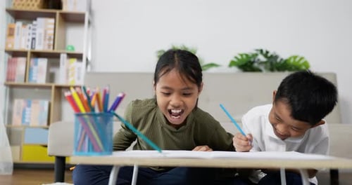 Two Children Drawing and Laughing Together Indoors