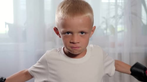 Porträt eines kleinen Jungen in einem roten Boxhandschuh zu Hause in der Nähe des Fensters