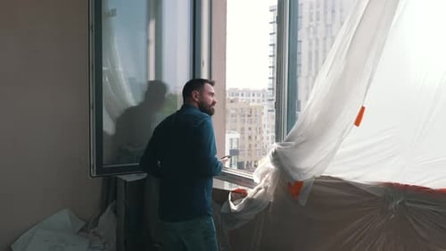 Bearded Man Looks out Apartment Window with Phone