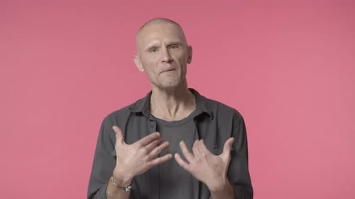 Mature Adult Talking and Gesturing Against Pink Backdrop
