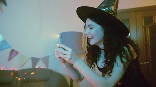 Woman in Witch Costume Looks at Phone and Laughs