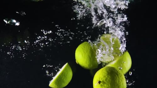 Limes Splashing into Water on Black Background