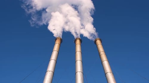 Industrial Smokestacks Emitting White Smoke Against Blue Sky