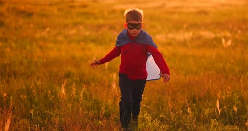 Little Superhero Boy in the Field at Sunset Fantasizes and Dreams.