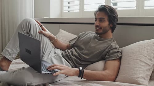 Young Man Relaxing on Bed Using Laptop