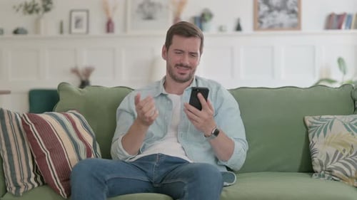 Upset Man Using Smartphone on Couch at Home