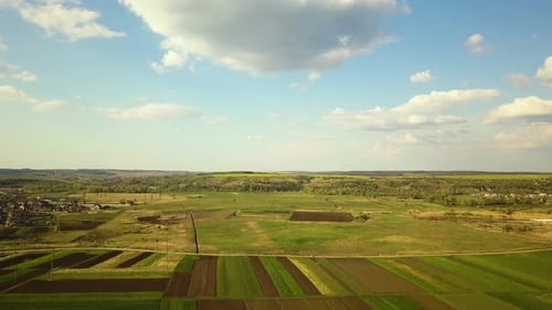 Aerial view of pathed plowed farm fields and distant village houses in spring.