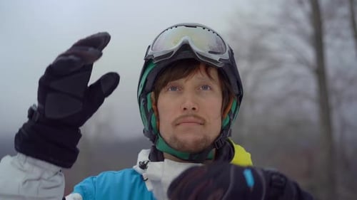 Closeup Shot of a Young Man Wearing a Helmet with a Snowboard in a Mountain Resort. He Puts on His