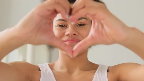 Woman Smiles and Makes Heart With Hands