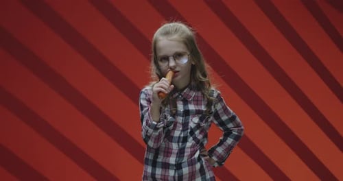Girl Eats Carrot in Front of Red Background