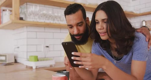 Smiling Couple Using Mobile Phone Together in Kitchen