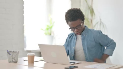 Young African Man Having Back Pain While Using Laptop in Office