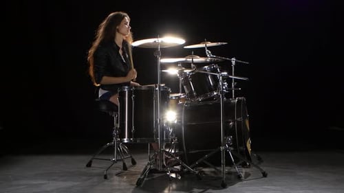 Woman Plays Drumset in Studio With Dramatic Lighting