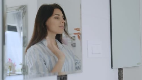 Woman Adjusts Hair in Bright Bathroom