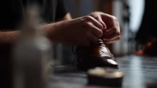 Closeup de sapateiro masculino amarrando cadarços em sapatos de couro marrom claro reparados e polidos