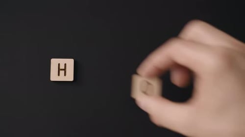 A close-up of a Caucasian hand placing carved wood letters that form the word ''home''