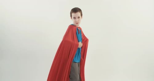 Boy with a superhero cape pretends to fly on a white studio background