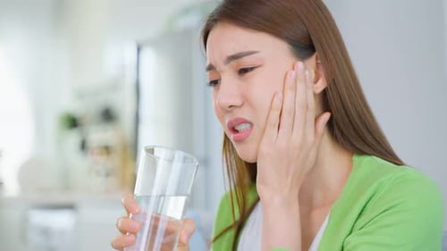 Asian beautiful woman sit on sofa in living room feel terrible toothache after drink cold water.