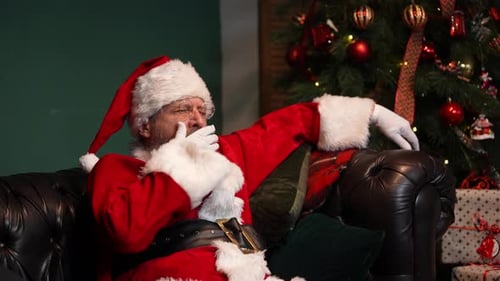 Tired Santa Claus Yawns and Falls Asleep Sitting on the Couch