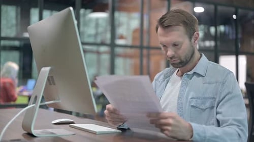 Man Reviews Documents in Front of Computer