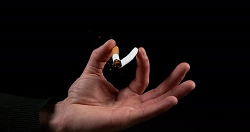 Main d'homme qui casse une cigarette sur fond noir, Ralenti 4K