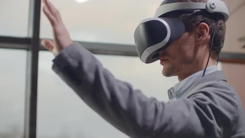 Man in a Helmet of Virtual Reality Against the Background of a Huge Window in the Office at the