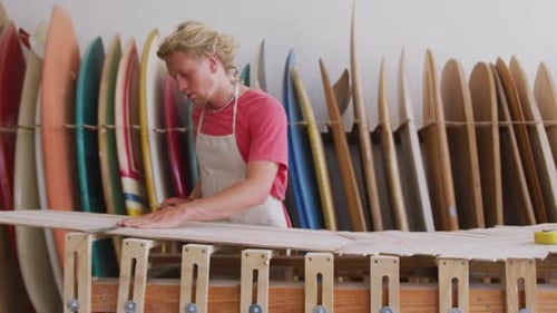 Caucasian male surfboard maker working in his studio and making a wooden surfboard