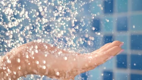 Weibliche Hand, die fließende Tropfen sauberen Kristallwassers aus der Dusche hält, Nahaufnahme, Zeitlupe