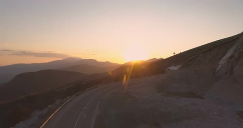 Drone Flying Towards Golden Sunset Following Winding Mountain Road