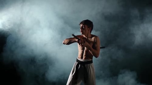 Karate-Mann mit einem nackten Torso Übung mit Nunchaku. Zeitlupe
