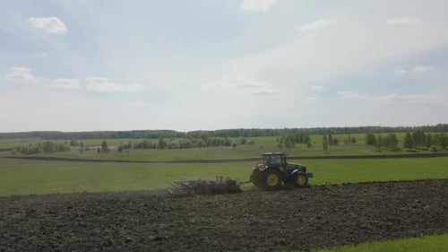 Un tracteur laboure la terre sur un champ vert non cultivé