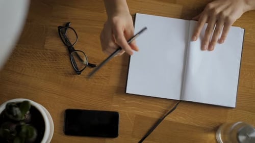 Hands Writing in Book on Wooden Table