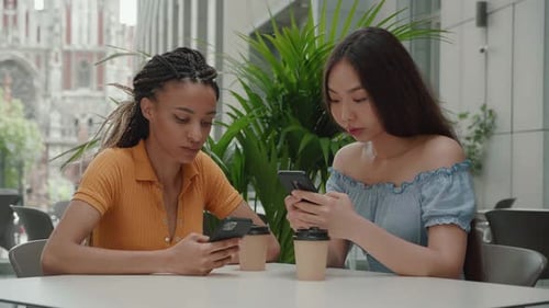 Asian and Mixed Race Young Girls Holding Smartphone Use Social Media Drink Coffee in Coffee Shop