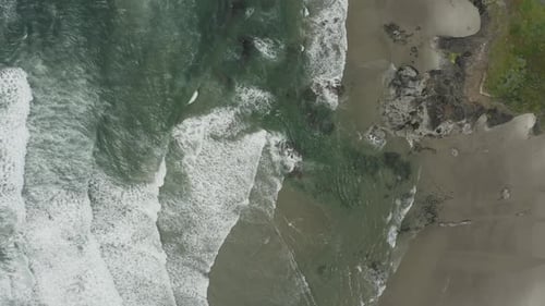 Left to right green and blue ocean waves crashing into ocean shore, peaceful drone video
