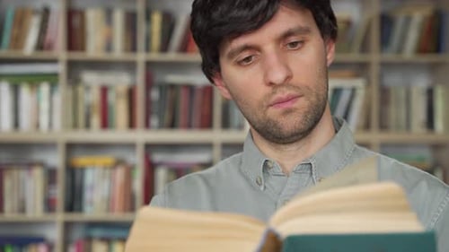 Young Male Student Reading a Book in a Library