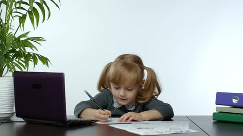 Girl Writes at Desk Next to Laptop and Plant