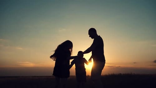 Silhouettes of happy family holding the hands in the meadow during sunset.