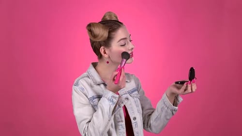 Girl Holding a Brush in Her Hand and Powdering Her Face. Pink Background