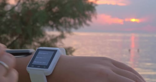 Woman Using Smartwatch at Sunset Over Ocean