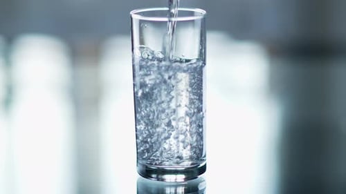 Pure water is poured into a glass beaker on a light background, close-up