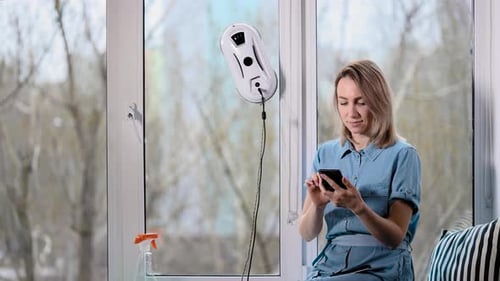 Jolie femme au foyer dans une robe bleue se repose et tape sur un smartphone