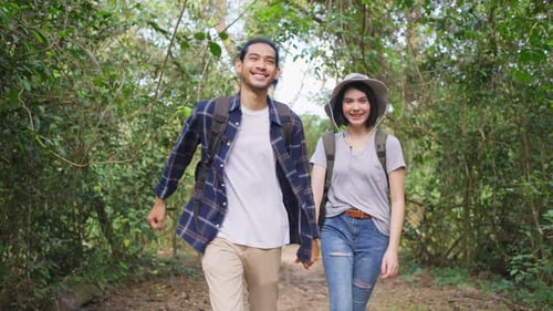 Young Asian man and Caucasian woman friend traveling and walking in the forest together on vacation.