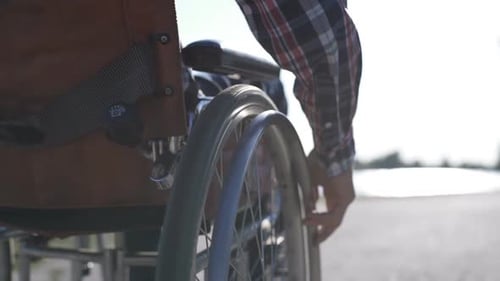 Person in Wheelchair Propels Along Path by Water
