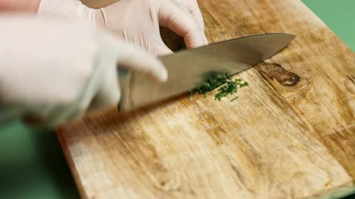 cutting parsley with knife above a wooden cutting board, side view