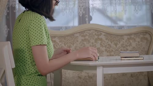 Side View of a Girl Reading a Book While Sitting at the Table