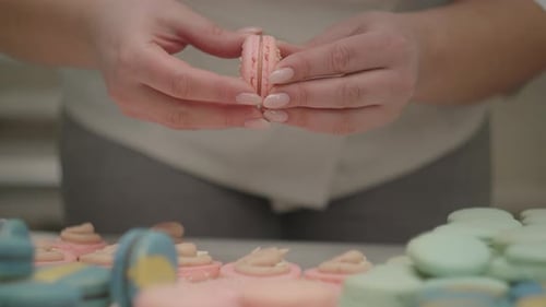 Woman's Confectioner's Hands Cooking Pink Macaron Cookies Placing Two Halves Together