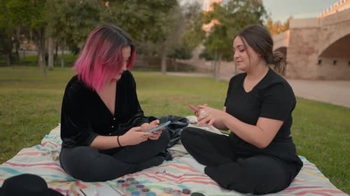 Young Women Sitting on Ground at Park Area Focusing on Smartphone Screen