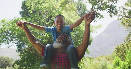 Adult Carrying Child on Shoulders in Green Space