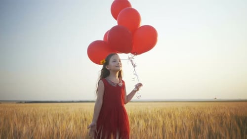 Happy Young Girl with Balloons Running in the Wheat Field at Sunset