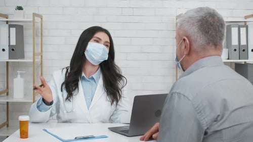 Female Doctor Consulting Senior Male Patient Sitting In Clinic Office